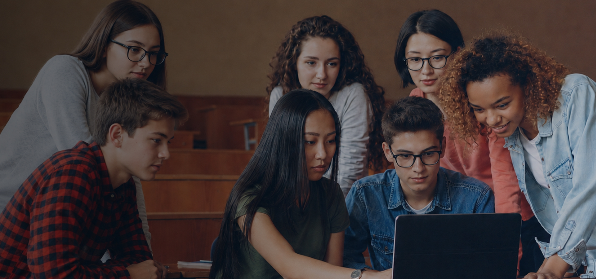 A diverse group of students collaborating around a laptop